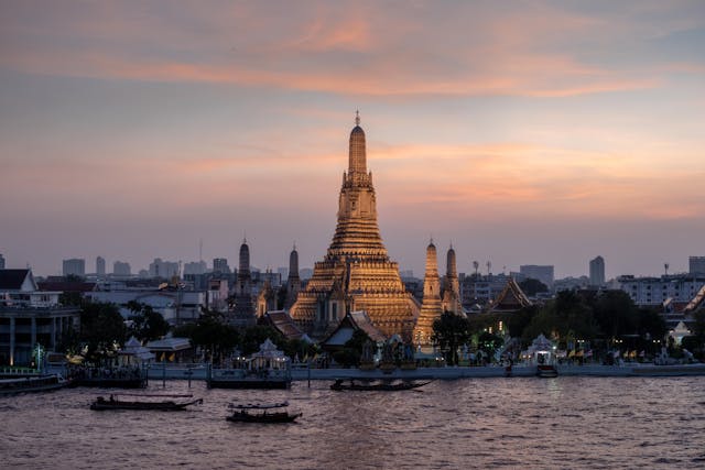 Templo Wat Arun al atardecer con luces doradas reflejadas en el río Chao Phraya.