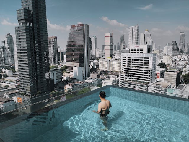Persona nadando en una piscina infinita con vista panorámica a los rascacielos de Bangkok bajo un cielo despejado.
