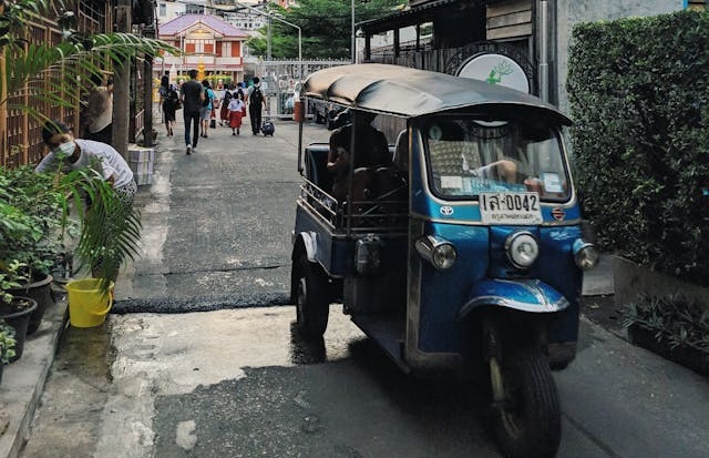 Un tuk-tuk azul circula por un estrecho callejón de Bangkok al atardecer.