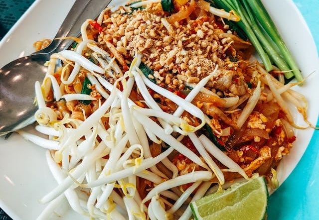 Plato de pad thai servido con brotes de soja, lima y cebollino en un plato blanco y azul.