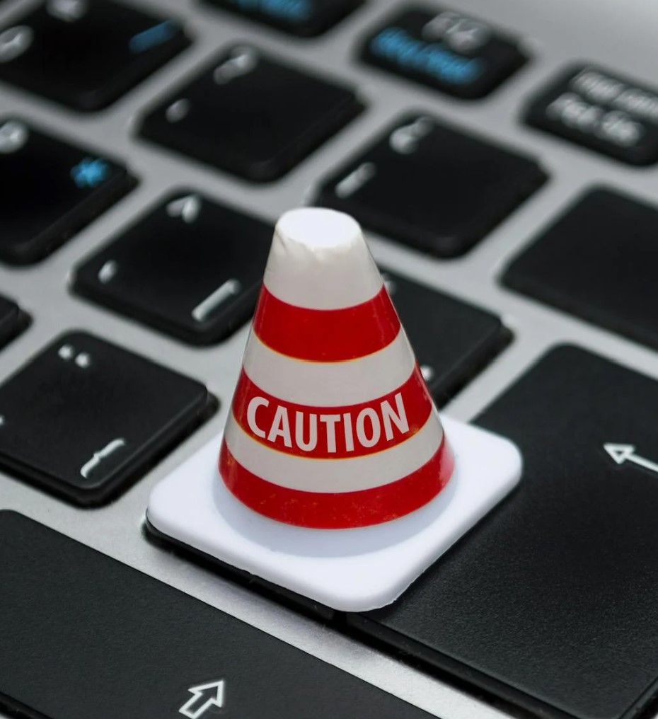 Un pequeño cono de advertencia con la palabra "CAUTION" colocado sobre un teclado de computadora, simbolizando precaución en el teletrabajo.