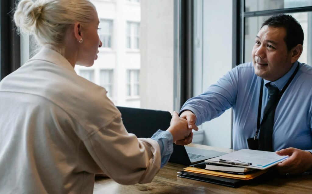 ersona estrechando la mano con un reclutador durante una entrevista de trabajo en una oficina.