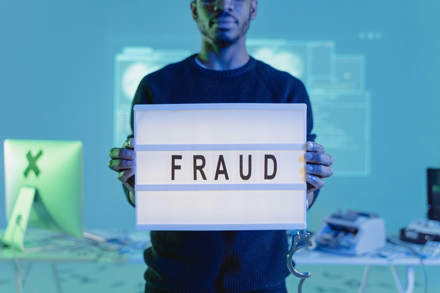Hombre sosteniendo un cartel iluminado con la palabra "FRAUD" en un entorno tecnológico, simbolizando el peligro de ofertas de trabajo falsas y esquemas piramidales.