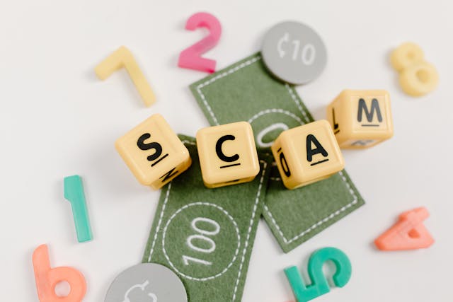 Letras formando la palabra "SCAM" sobre billetes y números de colores.