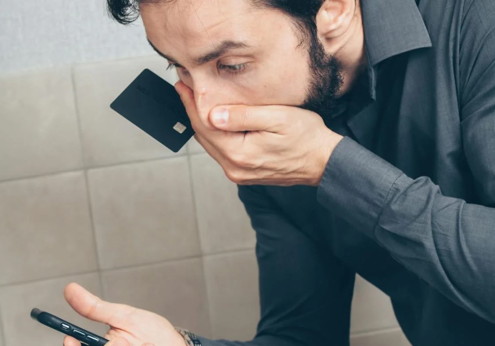Persona preocupada mirando un móvil mientras sostiene una tarjeta bancaria, reflejando el impacto de un posible fraude.