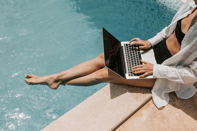 Mujer trabajando en una computadora portátil mientras se encuentra sentada al borde de una piscina.
