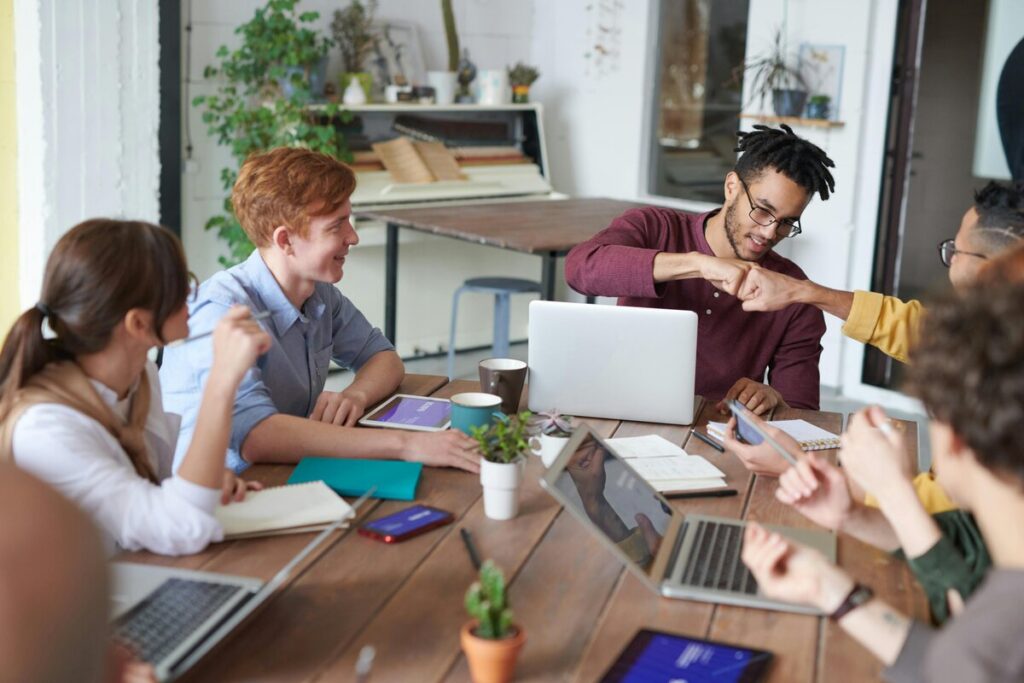 Un grupo de personas jóvenes colaborando en un espacio de trabajo moderno, compartiendo ideas y celebrando con un choque de puños.