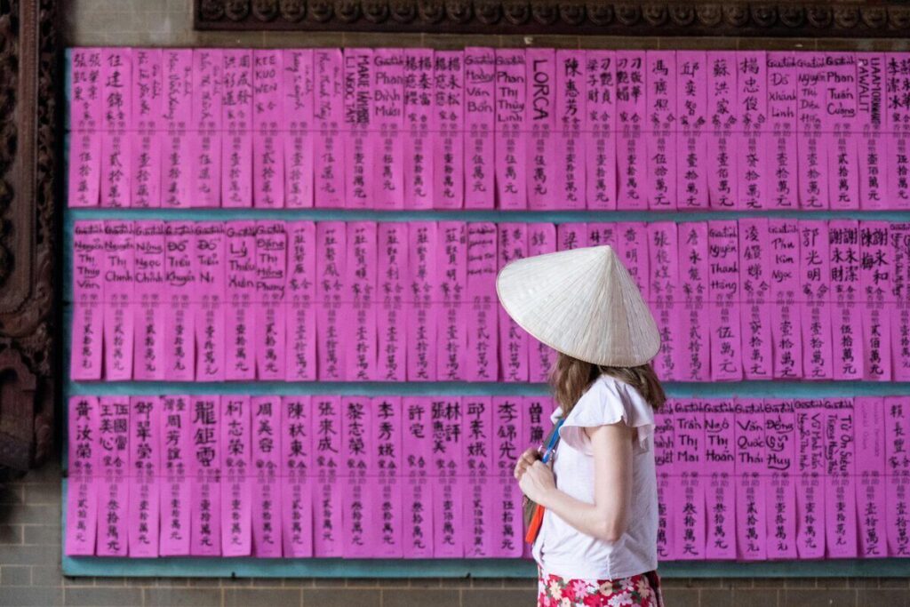 mujer con gorro vietnamita observando inscripciones hechas a mano en papeletas color fucsia