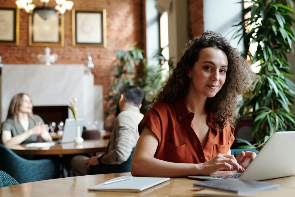 Mujer en cafetería con laptop y gente en el fondo